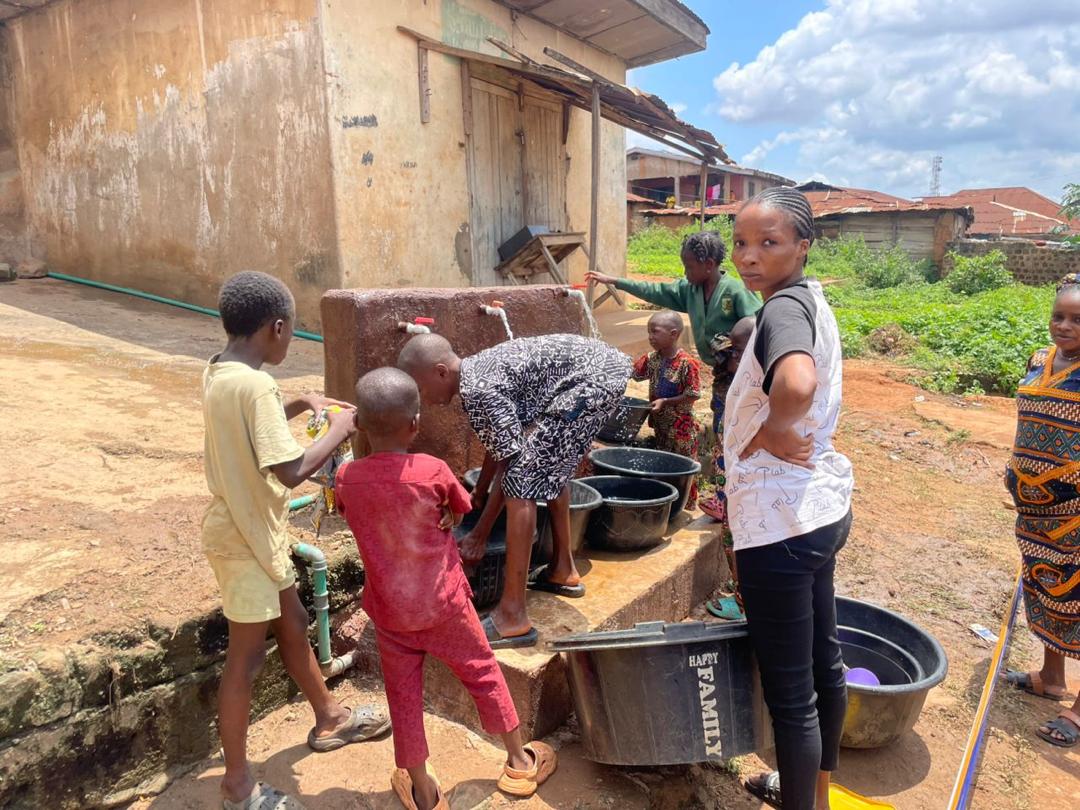 A woman looking directly at the camera while children fill containers