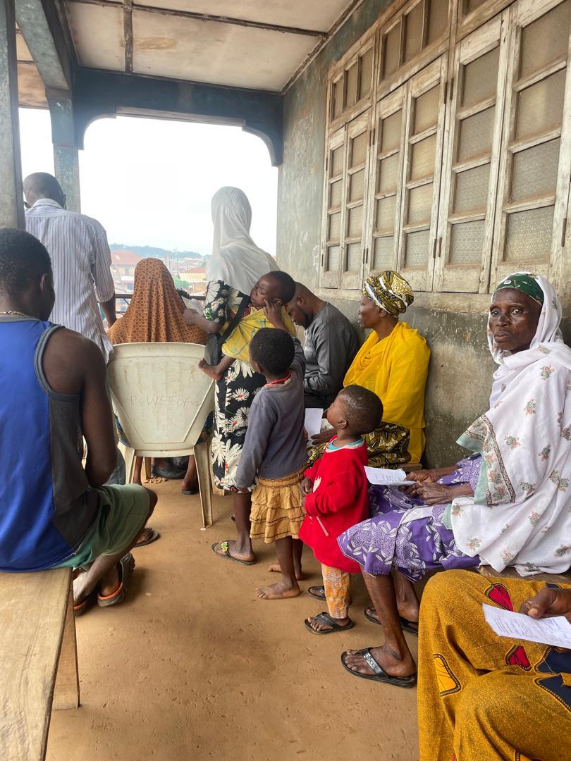 Residents of all ages seated along a covered corridor waiting to be seen
