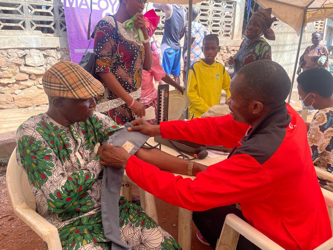 A volunteer checking an elderly man's blood pressure under the Mafoya banner